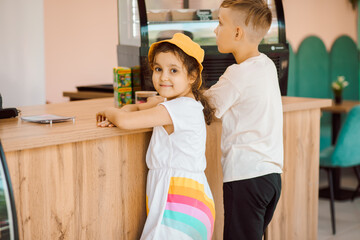 Cute girl and teenager boy buy waffles with ice cream and milkshake in cafe.