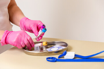Close up hands of nurse or medical worker in pink gloves with medical instruments for taking blood from vein on white background: syringe, bandage, tourniquet, test tube. Blood donation concept.