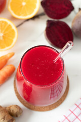 Red beetroot juice made with ginger, carrot, and lemon on white kitchen table. Healthy homemade blended drink.