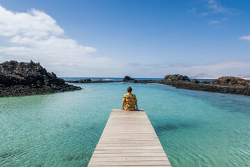 Tourist relaxing on a wooden pier in fuerteventura, canary islands, spain