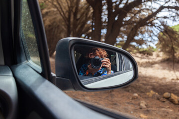 Photographer taking photos from car window reflected in side mirror