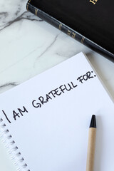 Handwritten text for gratitude in notebook with holy bible book on white marble table. Top view....