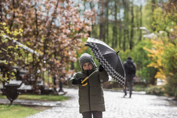 Fototapeta premium A small child of 5 years old with an umbrella in his hands during the spring rain. A spring break photo. A child under an umbrella.