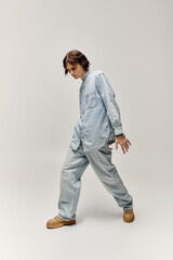 A handsome young man in denim attire strikes a fashionable pose, highlighting his trendy style.