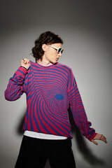 A stylish young man poses playfully in a vivid striped sweater and sunglasses.
