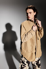 A handsome young man in stylish attire poses confidently, casting a striking shadow.