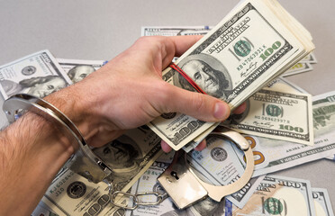 Folded hands and handcuffed hands resting on a table in front of money.