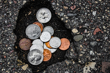 coins money in a pothole in the road abstract sunk costs unexpected costs metaphor bids...