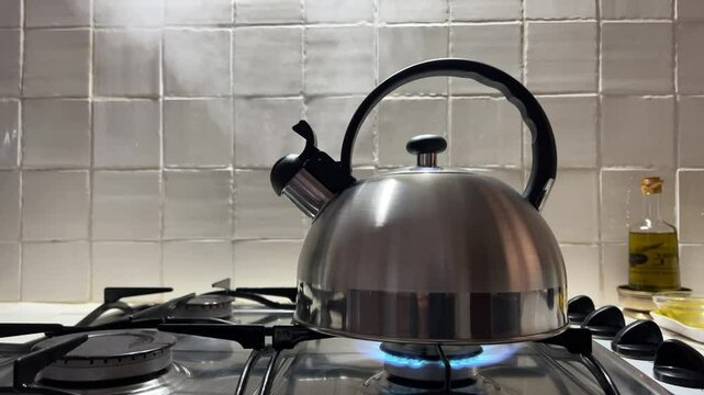 Una tetera de acero inoxidable con agua hirviendo  expulsando vapor caliente y pitando en una cocina de fuego de gas butano