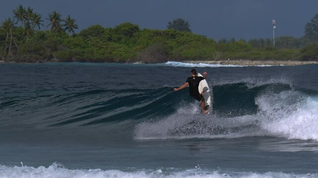 An adult male surfer catches a blue wave in the tropical waters of the Indian Ocean. A very hot sunny day.