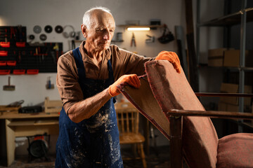 elderly craftsman restoring vintage chair in woodworking workshop