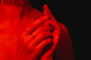 Tender hands intertwining beneath soft red illumination, expressing deep emotional connection and...