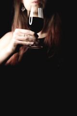 Woman wearing evening dress, holding red wine glass, standing against shadowy background, exuding sophisticated elegance book cover copy space
