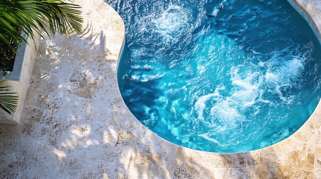 Top view of a vibrant blue pool with bubbling water surrounded by a stone patio and palm fronds