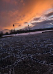A dramatic photograph capturing the interplay of light and shadow as the sun sets, casting long shadows across a cracked asphalt parking lot. A vibrant orange sky adds a touch of warmth to the scene