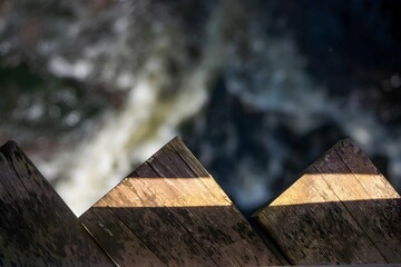 A close-up photograph of wooden planks with a blurred waterfall visible in the background, creating a sense of depth and mystery