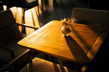 A close-up photograph of a wooden cafe table bathed in warm sunlight, with a small vase of flowers adding a touch of elegance