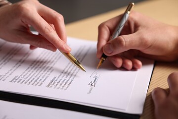 Naklejka premium Woman pointing at document and man putting signature at table, closeup