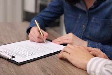 Woman putting signature on document at wooden table, closeup