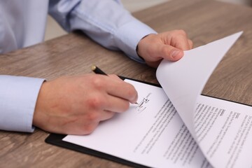 Man putting signature on document at wooden table, closeup