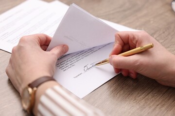 Fototapeta premium Woman putting signature on document at wooden table, closeup
