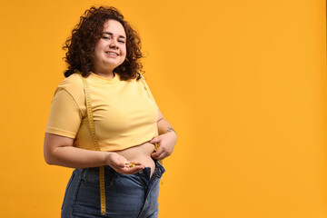 Happy plus size woman with pile of weight loss supplements on orange background. Space for text