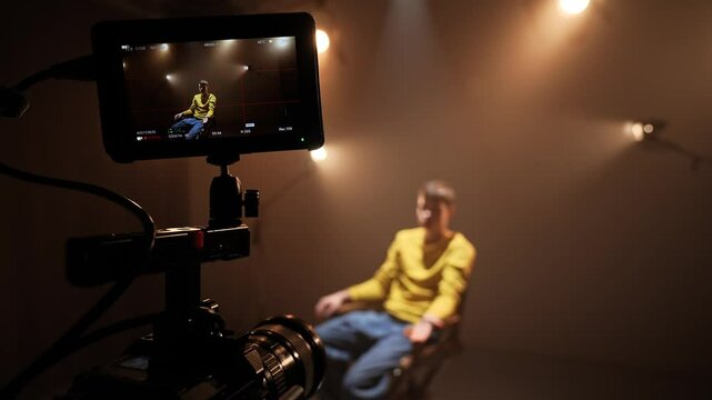 Studio for photo video production filming with lighting equipment and cyclorama, close shot focus on camera display recording actor sitting on chair and talking.
