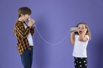Boy and girl talking on tin can telephone against violet background