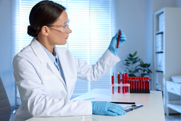 Laboratory testing. Doctor holding test tube with blood sample at table indoors