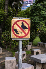 a sign in a park that prohibits feeding pigeons. The sign is a red circle with a diagonal line...
