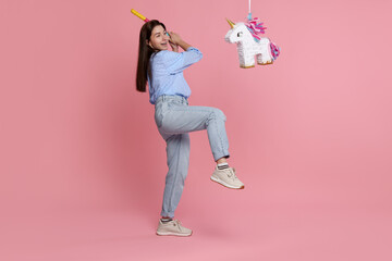 Happy woman hitting unicorn shaped pinata with stick on pink background © New Africa