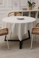 Table with white tablecloth, plates and chairs in stylish room. Interior design