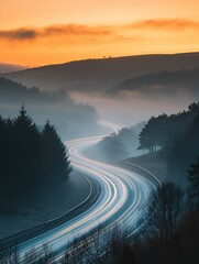 Winding road through misty hills at sunrise with light trails from passing cars in the morning