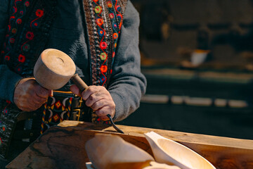 A skilled artisan, wearing a colorful garment, carefully carves wooden bowls with a mallet and chisel in a warm, rustic workshop setting.