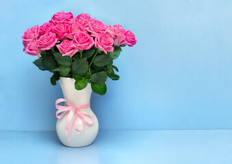 Bouquet pink flowers roses in white porcelain vase on a white table on blue background with space for text