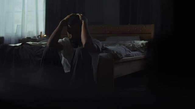 Despaired African American man cries on floor in dark bedroom