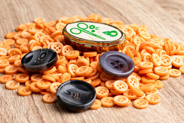 tres botones grandes grises y una pequeño costurero sobre un lote de botones plásticos naranjos