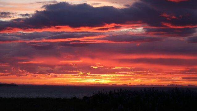 A breathtaking sunset paints the sky with vibrant shades of red, orange, and purple over a serene coastal landscape. 