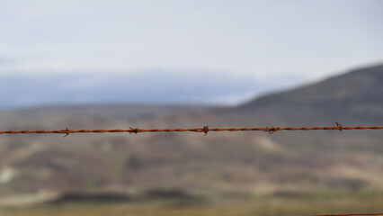 A close-up of a rusted barbed wire fence set against a blurred mountainous landscape