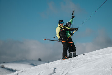Two people ride a ski lift on a snowy mountain slope. Wearing ski gear, they enjoy a winter sport activity under clear and sunny blue skies, symbolizing adventure, recreation, and outdoor enthusiasm.