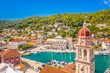 A scenic view of Pučišća on Brac Island, Croatia, featuring the church bell tower and waterfront, with the entire charming fishing village in the background, bathed in warm sunlight