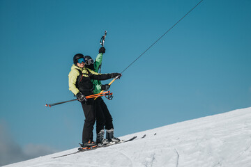 Two skiers dressed in winter attire joyfully riding a ski lift up a snowy slope on a clear sunny day, surrounded by the picturesque alpine scenery and displaying excitement for outdoor sports.