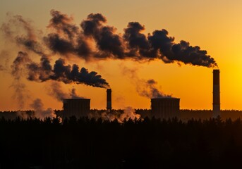 Fototapeta premium Power plant with dark smoke emissions against an orange sky during a scenic sunset view