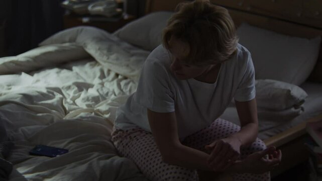 Woman in pajamas scared by ringing call sits in bedroom