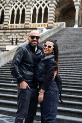  Happy smiling beautiful  Tourists  couple traveling in Italy poses and making photos near the Cathedral of Amalfi  .Family on vacation on Amalfi coast in Italy. 