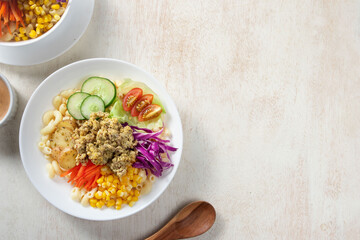 Vegetable salad, Colorful bowl filled with grains, fresh vegetables, and crispy topping, accompanied by a small bowl of dipping sauce on a light surface