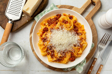 Plate with pappardelle bolognese and parmesan cheese, italian egg pasta with meat ant tomato ragu sauce. Top view on a white table.