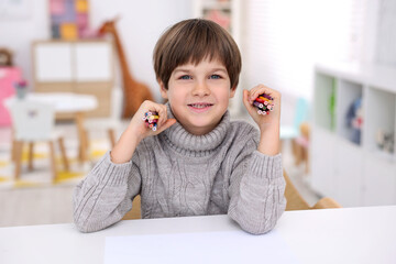 Portrait of smiling boy with colorful pencils at white table in kindergarten
