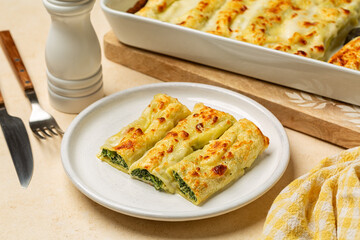 Lunch with Baked Cannelloni, cylindrical type of egg-based pasta stuffed  with spinach and ricotta, covered by cheese and bechamel  sauce in Italian cuisine. Beige table.