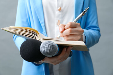 Journalist with microphones taking notes on grey background, closeup